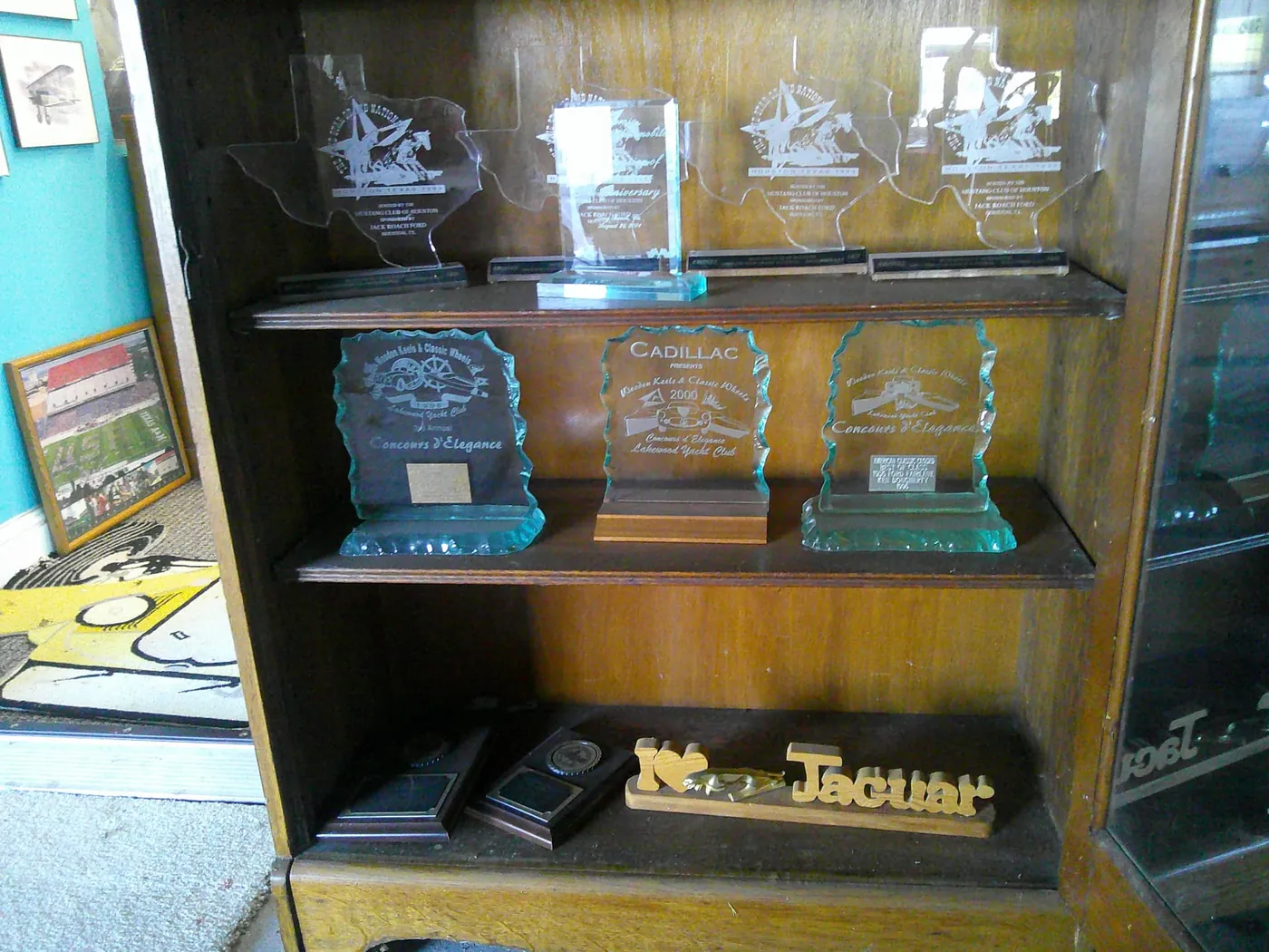 Etched glass Concours d'Elegance awards and Texas-shaped Mustang Club trophies on display.